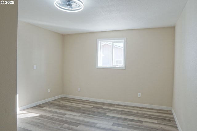 spare room featuring a textured ceiling, light wood-type flooring, and baseboards