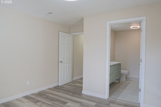 unfurnished bedroom featuring ensuite bathroom, baseboards, visible vents, and light wood finished floors