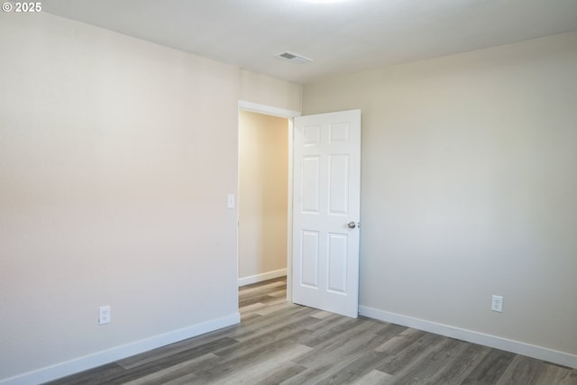 empty room with wood finished floors, visible vents, and baseboards