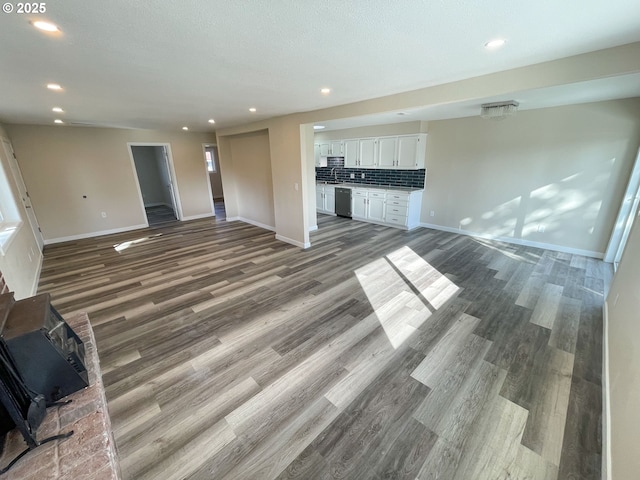 unfurnished living room featuring recessed lighting, baseboards, wood finished floors, and a wood stove