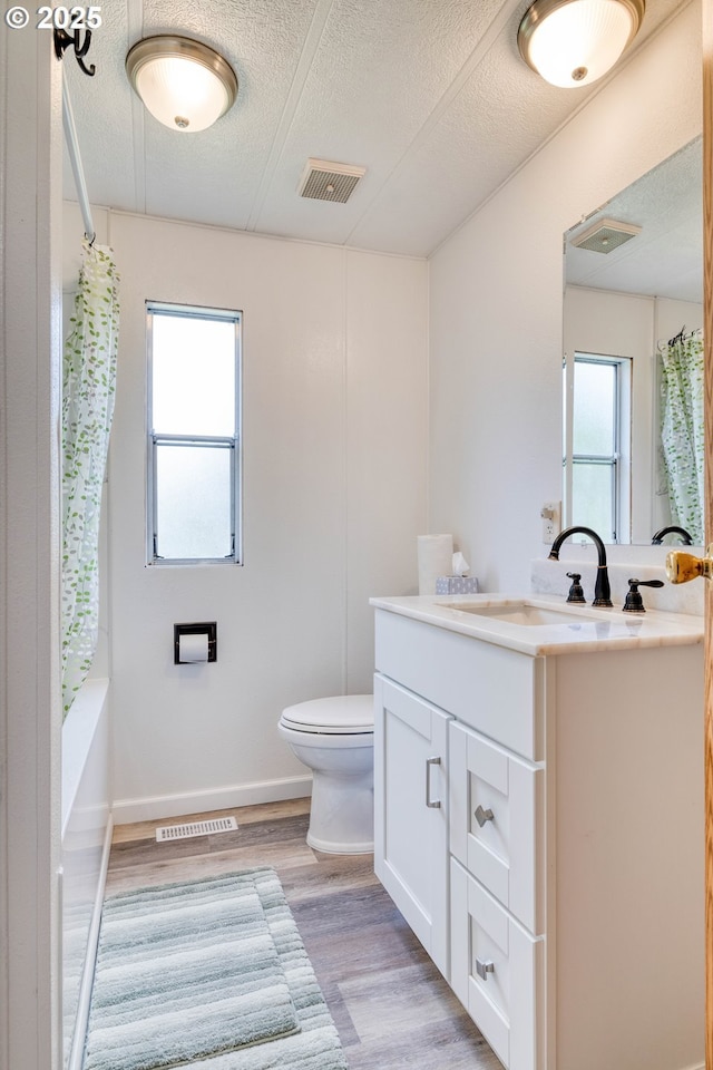 bathroom featuring toilet, wood finished floors, a textured ceiling, vanity, and shower / bathtub combination with curtain
