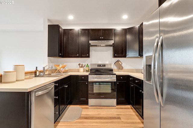kitchen featuring appliances with stainless steel finishes, under cabinet range hood, a sink, recessed lighting, and light wood-style floors