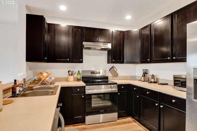 kitchen featuring stainless steel appliances, under cabinet range hood, a sink, light countertops, and light wood-style floors