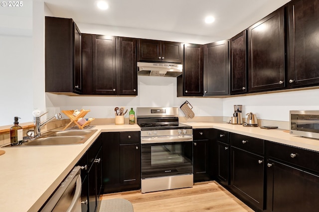 kitchen featuring appliances with stainless steel finishes, under cabinet range hood, a sink, light countertops, and recessed lighting