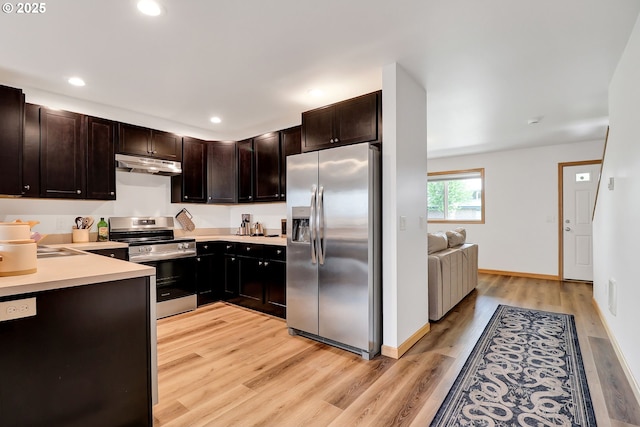 kitchen featuring stainless steel appliances, under cabinet range hood, light wood finished floors, dark brown cabinets, and light countertops