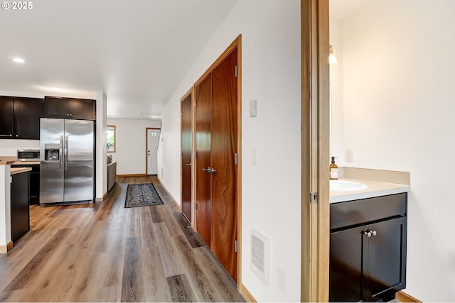 kitchen featuring appliances with stainless steel finishes, light wood-type flooring, light countertops, dark brown cabinets, and baseboards