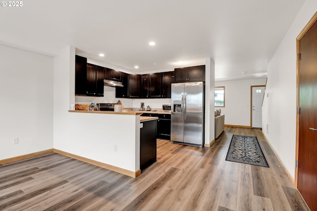 kitchen with stainless steel fridge with ice dispenser, light wood-type flooring, light countertops, under cabinet range hood, and recessed lighting