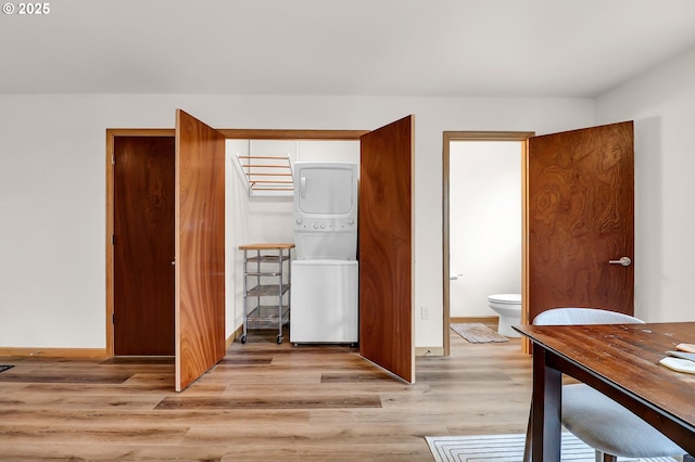 bedroom featuring stacked washer / drying machine, light wood-style floors, baseboards, and ensuite bathroom