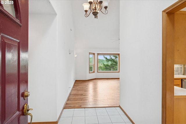 foyer featuring light tile patterned flooring, a chandelier, a high ceiling, and baseboards