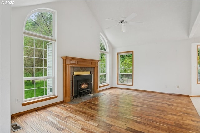 unfurnished living room with a wood stove, wood finished floors, plenty of natural light, high vaulted ceiling, and baseboards