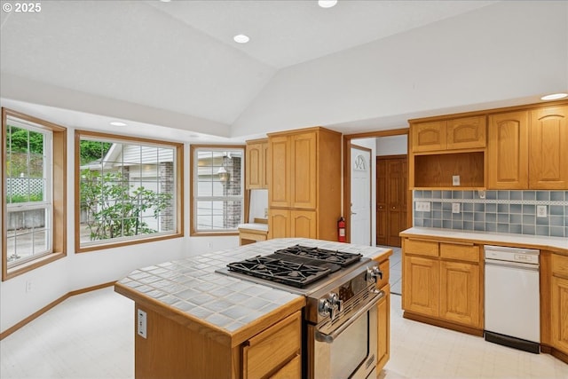 kitchen featuring tile counters, stainless steel gas range, lofted ceiling, light flooring, and a kitchen island