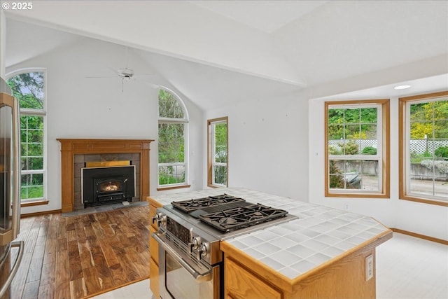 kitchen with tile countertops, stainless steel range with gas stovetop, healthy amount of natural light, and lofted ceiling