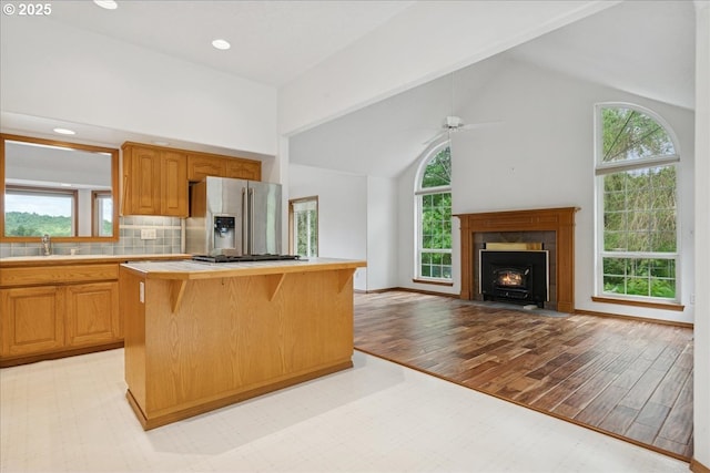 kitchen with stainless steel fridge with ice dispenser, light countertops, a kitchen island, healthy amount of natural light, and high vaulted ceiling