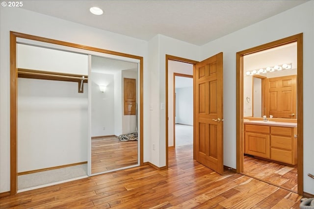 unfurnished bedroom with light wood finished floors, a closet, baseboards, a sink, and ensuite bath