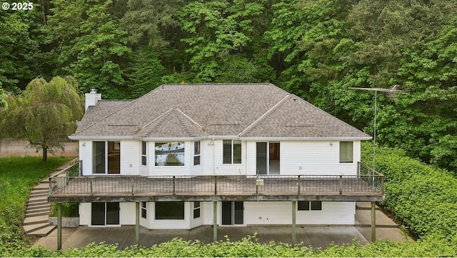 rear view of property featuring a patio area, a chimney, a deck, a forest view, and roof with shingles