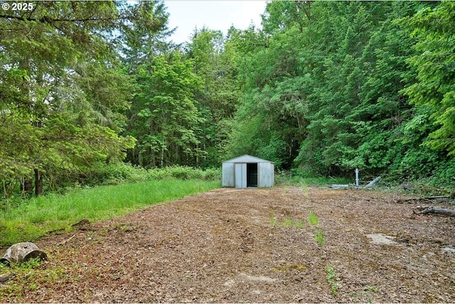 view of yard featuring a storage shed, an outdoor structure, and a wooded view