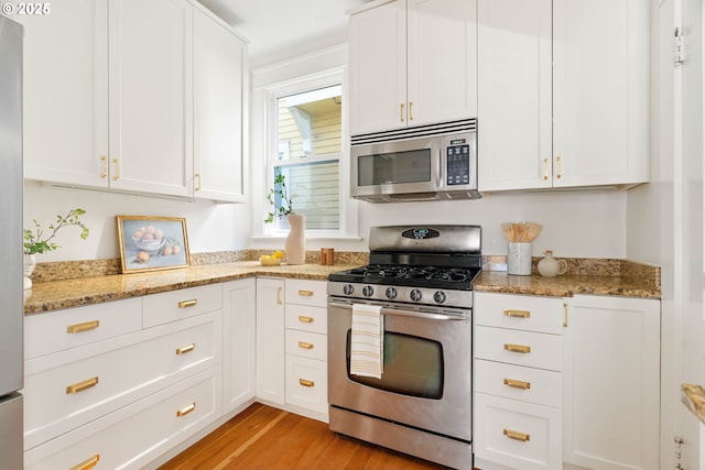 kitchen with stainless steel appliances, white cabinets, light wood finished floors, and light stone counters