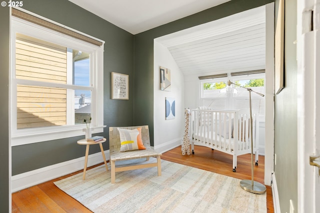 bedroom with vaulted ceiling, wood finished floors, baseboards, and a nursery area