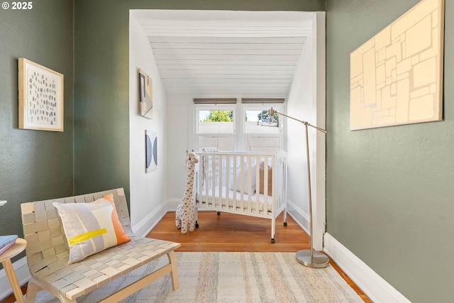 bedroom with wood finished floors, baseboards, a nursery area, and vaulted ceiling