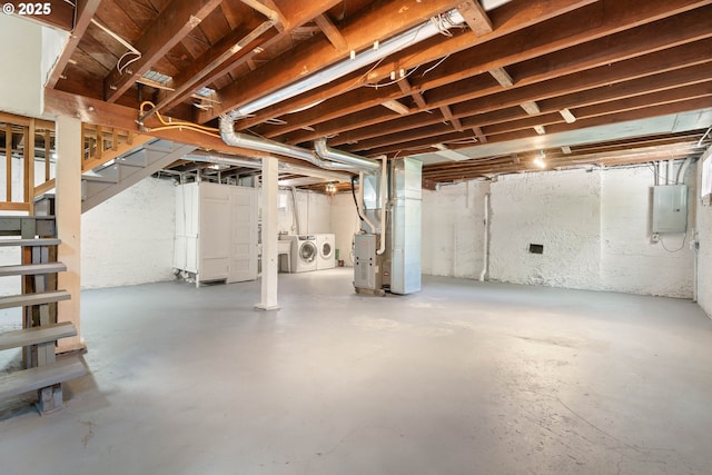 unfinished basement featuring washing machine and dryer, electric panel, heating unit, and stairway