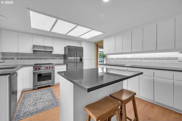 15645 NE Russell Pl, Portland, OR 97230 - kitchen with premium appliances, a breakfast bar area, decorative backsplash, under cabinet range hood, and light wood finished floors