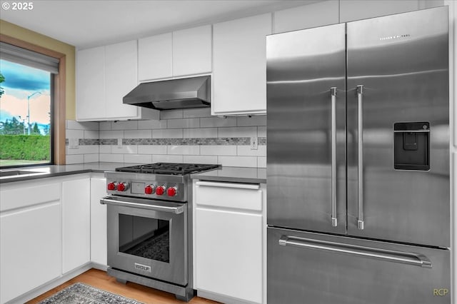 15645 NE Russell Pl, Portland, OR 97230 - kitchen with high end appliances, range hood, white cabinetry, backsplash, and dark countertops