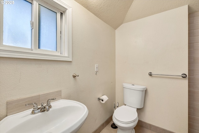 bathroom with toilet, sink, vaulted ceiling, a textured ceiling, and tile patterned flooring