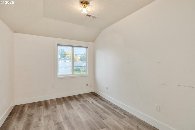 spare room featuring vaulted ceiling, a textured ceiling, and light hardwood / wood-style floors