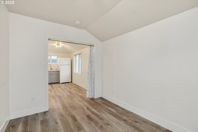 empty room featuring lofted ceiling, sink, and light hardwood / wood-style flooring