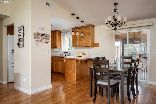 dining space featuring visible vents, light wood-style flooring, baseboards, and an inviting chandelier