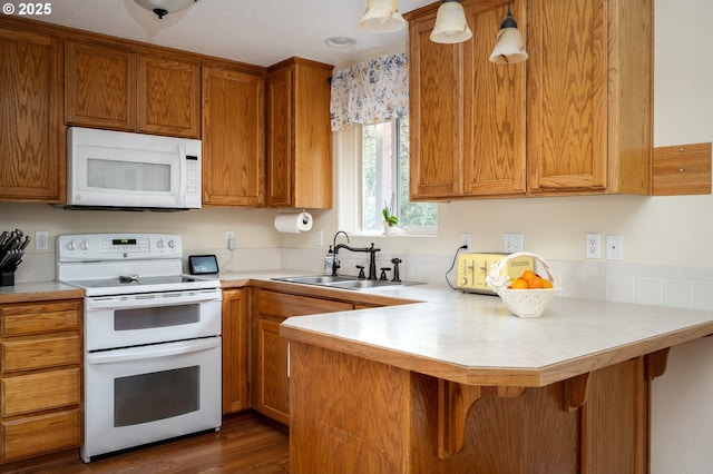 kitchen featuring brown cabinets, a sink, white appliances, a peninsula, and light countertops