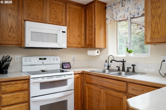 kitchen with a sink, white appliances, brown cabinets, and light countertops