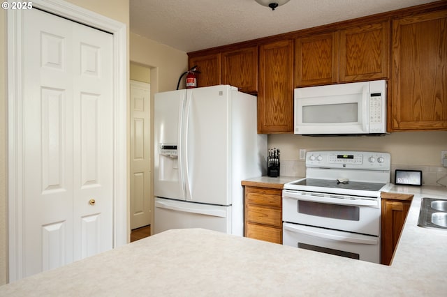 kitchen featuring white appliances, brown cabinetry, light countertops, and a textured ceiling