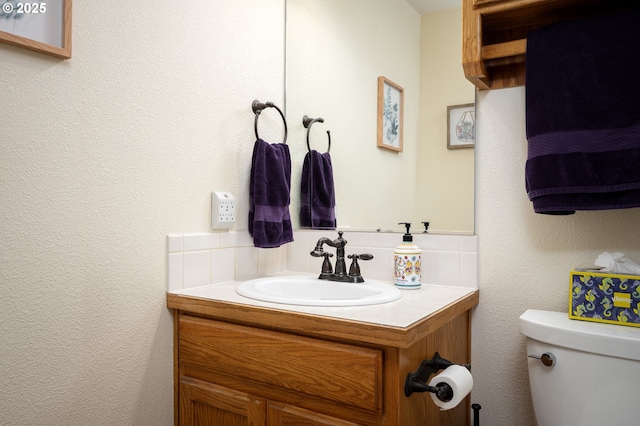 bathroom featuring vanity, toilet, and a textured wall