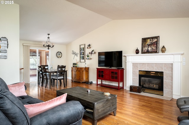 living room with baseboards, a chandelier, a tiled fireplace, lofted ceiling, and light wood-style flooring