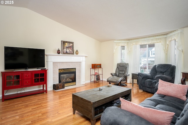 living room featuring a tile fireplace, baseboards, lofted ceiling, and wood finished floors