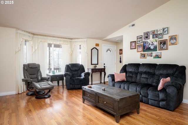 living room with light wood-type flooring, visible vents, lofted ceiling, and baseboards