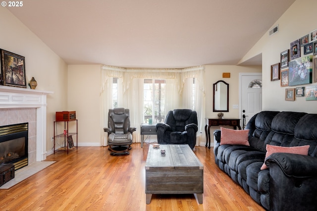 living room with visible vents, baseboards, lofted ceiling, light wood-style flooring, and a fireplace