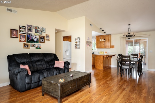 living area with baseboards, visible vents, light wood finished floors, vaulted ceiling, and a chandelier