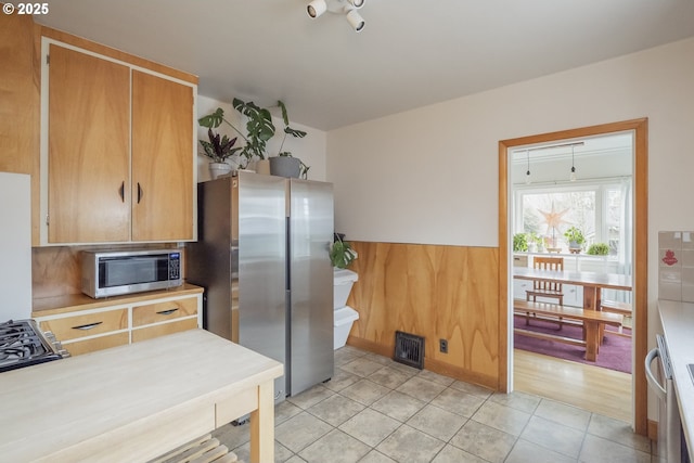 kitchen with light tile patterned floors, stainless steel appliances, and wood walls