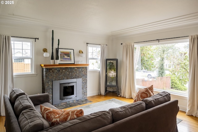 living room featuring a tiled fireplace, crown molding, and light wood-type flooring