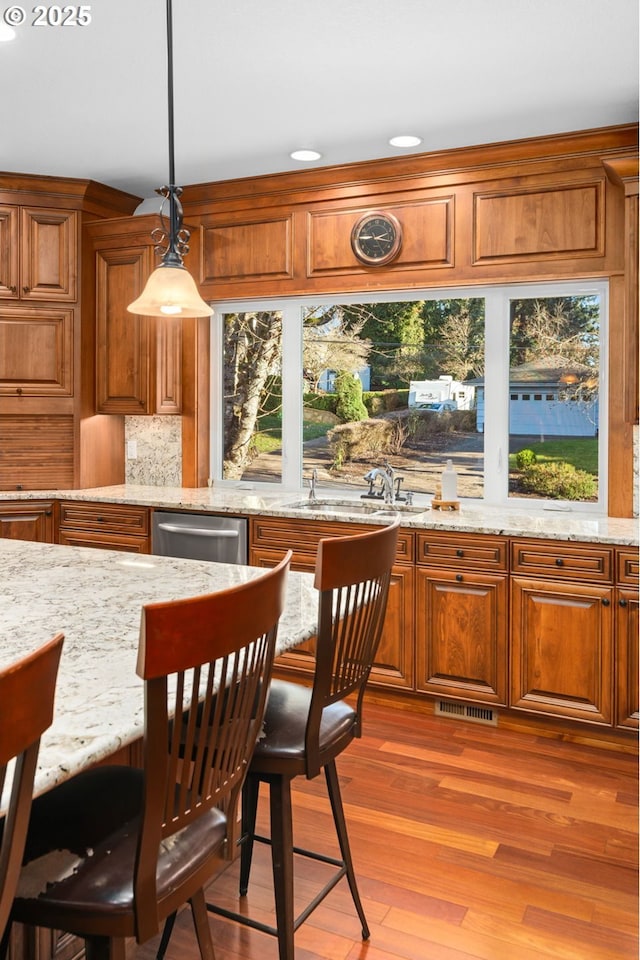 kitchen featuring light wood-style flooring, light stone countertops, brown cabinetry, dishwasher, and a sink