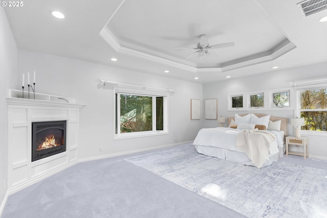 carpeted bedroom with a warm lit fireplace, a tray ceiling, baseboards, and visible vents