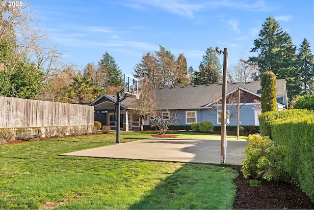 back of property with fence, basketball hoop, and a lawn