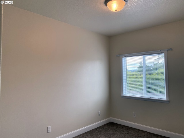 empty room with dark colored carpet, baseboards, and a textured ceiling