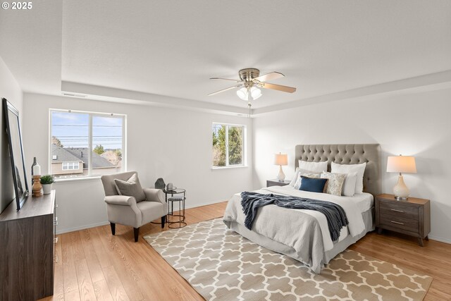 bedroom featuring ceiling fan, a raised ceiling, and light hardwood / wood-style flooring