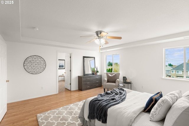 bedroom with ceiling fan, a tray ceiling, and light hardwood / wood-style floors