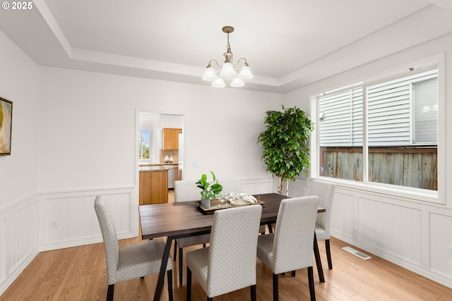 dining room featuring an inviting chandelier, a raised ceiling, and light hardwood / wood-style flooring