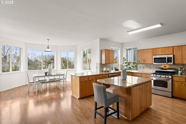 kitchen with decorative light fixtures, light wood-type flooring, appliances with stainless steel finishes, a kitchen island, and backsplash