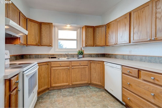 kitchen with under cabinet range hood, white appliances, a sink, brown cabinets, and stone finish floor